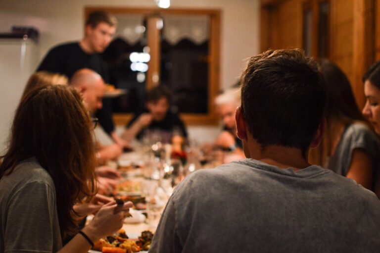 Guests seated around a long dinner table at Chalet Atelier with the chef preparing food in the background.