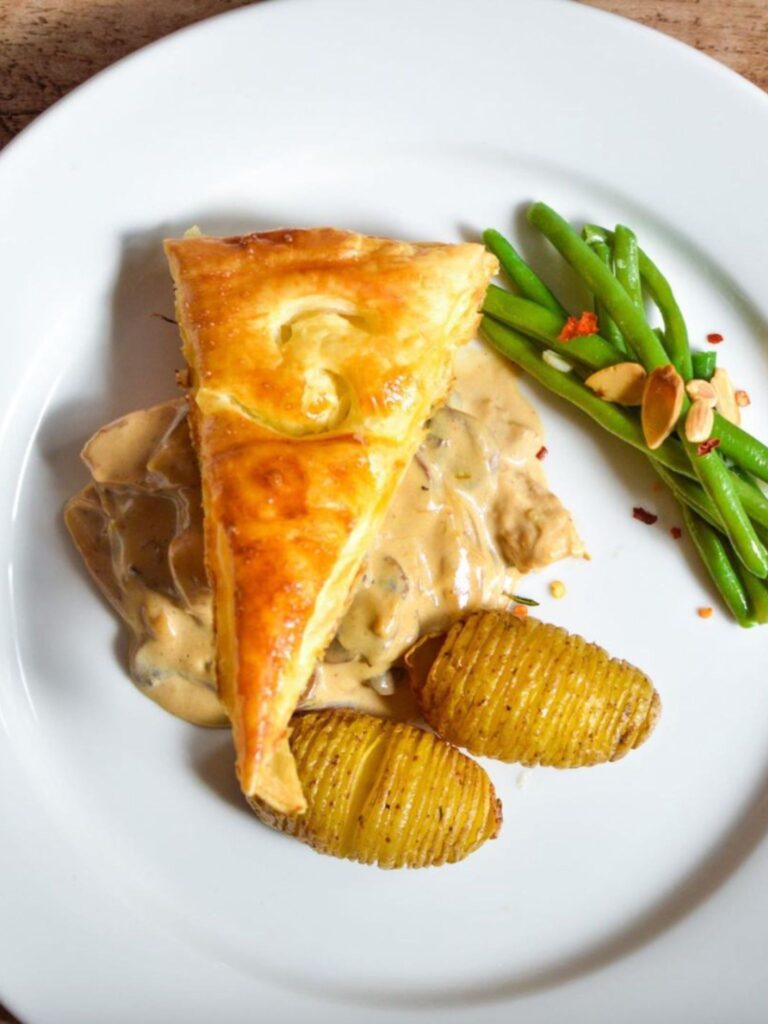 Claridges Chicken Pie A slice of golden chicken pie served with crispy potatoes, creamy chicken filling, and green beans on a white plate.